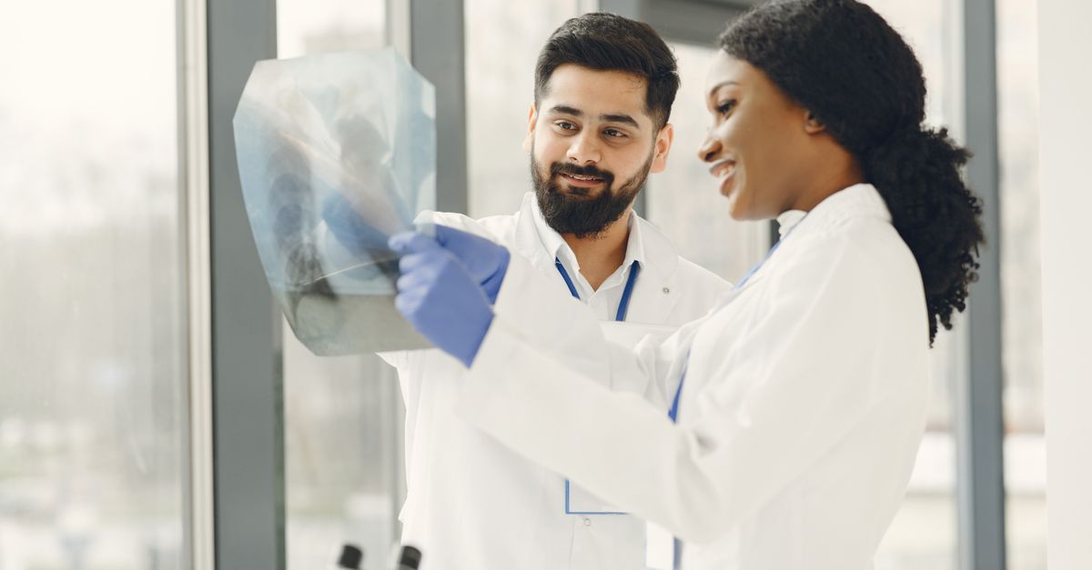 Two doctors in lab coats examine an X-ray image in a bright medical facility.